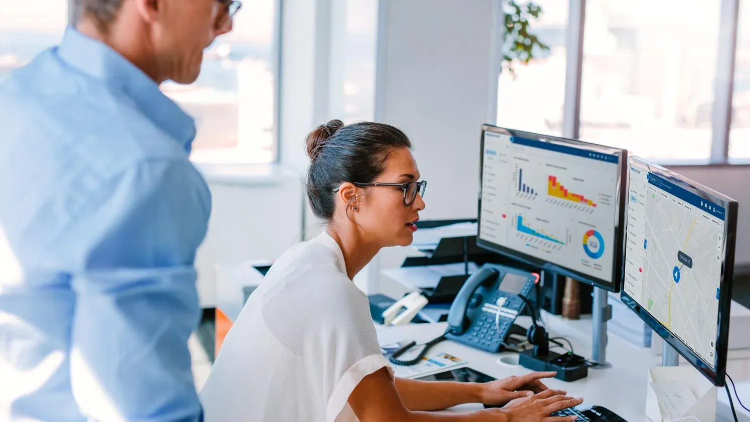 A professional woman monitors vehicle tracking and performance data on the Geotab dashboard, with a colleague reviewing the information.