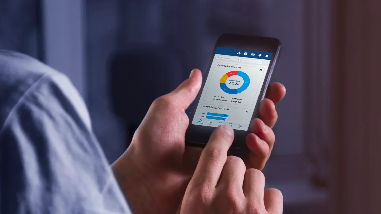 A close-up of a hand holding a smartphone showing driver safety scorecards and fleet mileage data, part of Geosecure's telematics solution. 